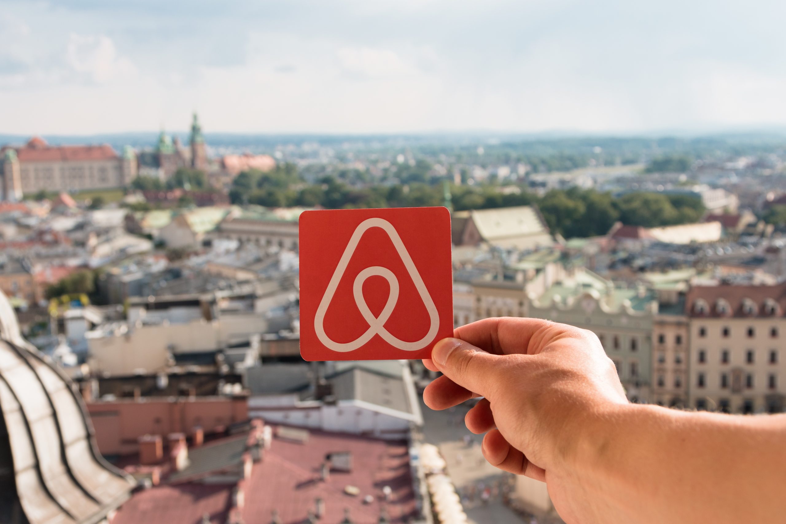 Krakow, Poland - July, 2017: Travel around the world with Airbnb. Logo Airbnb and the city on the background. Home concept. Man holds the logo of a popular company.